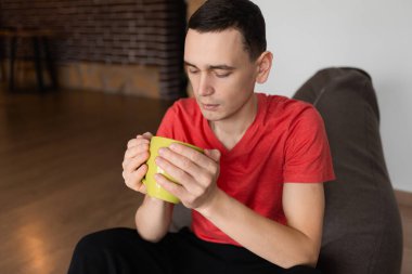 Genç hippi oturma odasında elinde bir kupa çayla oturuyor.