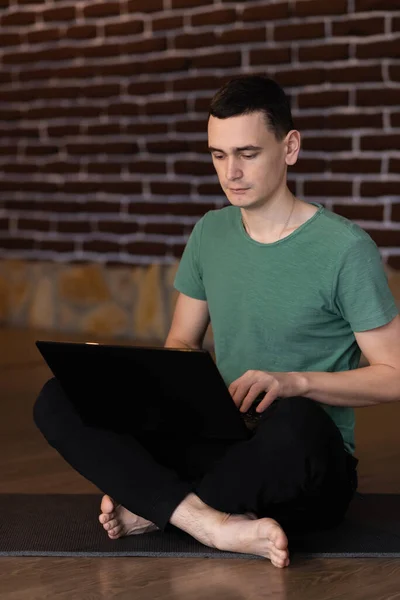 Student sitting on floor of his apartment with laptop and notes studying