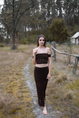 Çıplak ayaklı kadın güzel bir gece elbisesiyle orman yolunda yürüyor.