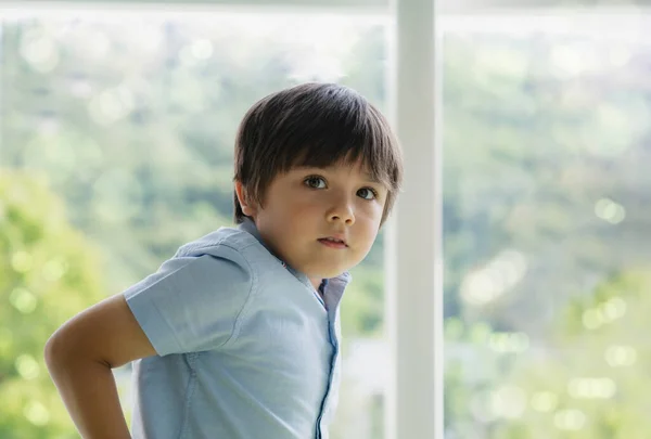 High key light Portrait handsome kid standing next to window looking at camera with smiling face. Positive child boy relaxing on weekend in sunny day spring or summer