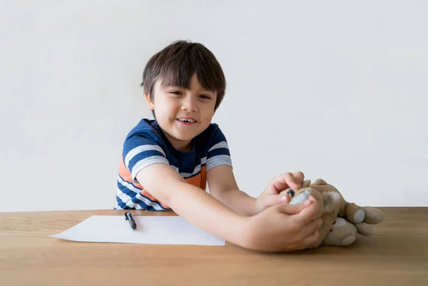 Happy kid playing with dog toy while doing homework, Child  playing with his soft toy on the table, A boy enjoying his free time at home. Elementary school and homeschooling concept