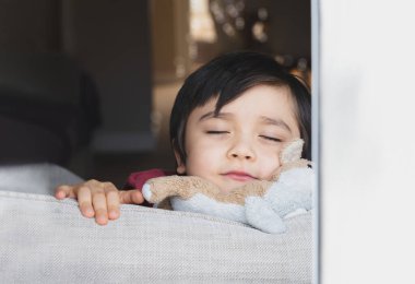 Mutlu Çocuk gözlerini kapatıyor, pencerenin kenarında gülümsüyor, pozitif çocuk kasvetli bir günde oturma odasında dinleniyor, tatlı çocuk hafta sonları evde dinleniyor.. 