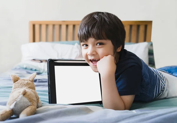 Kid laying in bed with dog toy and looking up at camera,Cute child boy lying in bed with tablet,Top view Children playing alone in bedroom with mock up of digital tablet.New normal lifestyle