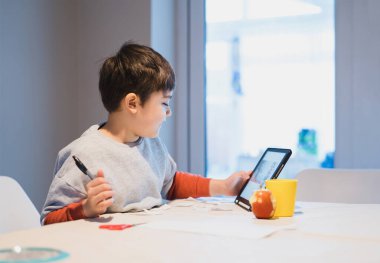 Ödevlerinde tablet kullanan anaokulu çocuğunun orijinal portresi, yeni normal çocuk evde öğrenme, E-öğrenme ya da evde eğitim konsepti için dokunmatik ped kullanıyor