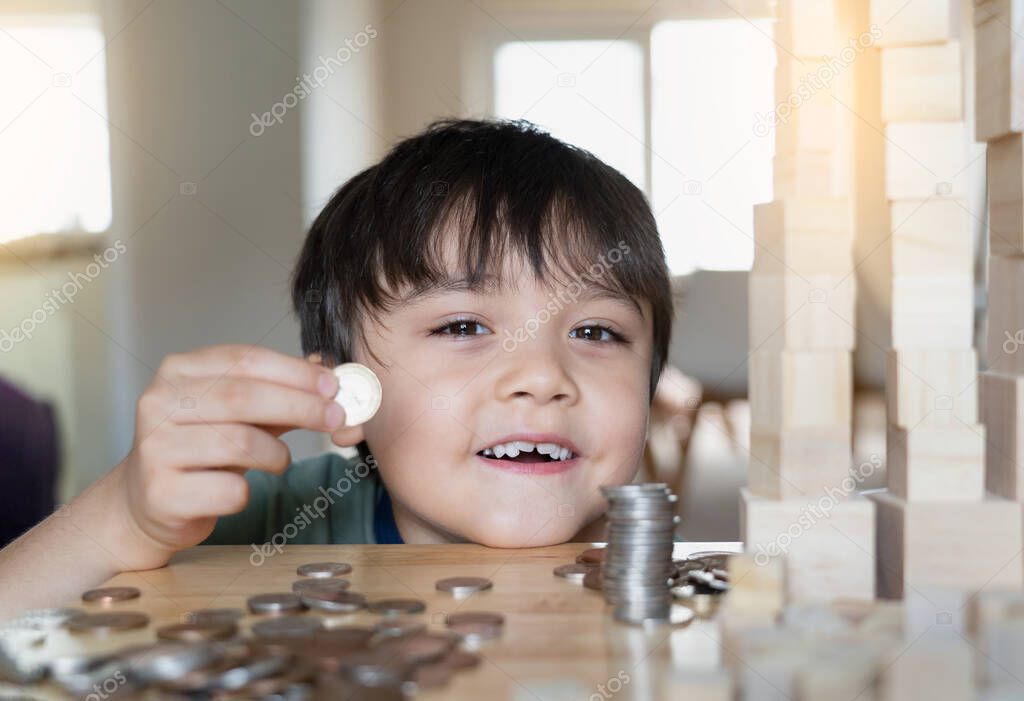 Selective focus kid holding money coin on his hand with smiling face with blurry foreground of coin on table. Child boy with smiling face counting money Learning financial responsibility and saving 