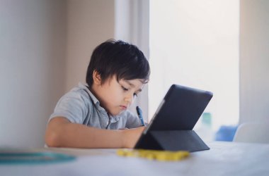 Portrait of preschool kid using tablet for his homework, Child doing homework by digital tablet searching information on internet, E-learning or Home schooling education concept
