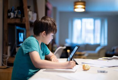 Elinde kağıt kalem tutan çocuk, internette dijital tablet kullanarak ev ödevi için bilgi arayan çocuk, evde eğitim, e-öğrenim online eğitim