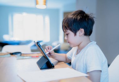 Çocuk tablet üzerinde dijital kalem kullanıyor, Otantik Genç çocuk ödevi için dijital ped kullanıyor, Çocuk öğretmenle online zoom video çalışması yapıyor, evde eğitim, E-öğrenim online eğitim