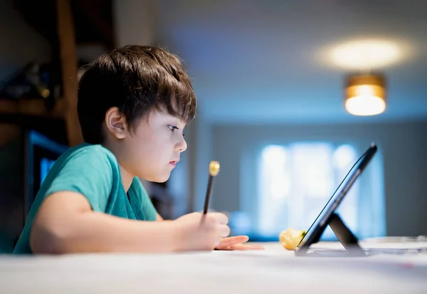 Kid holding pencil wring on paper, Child using digital tablet searching information on internet for his homework, Home schooling, E-learning online education