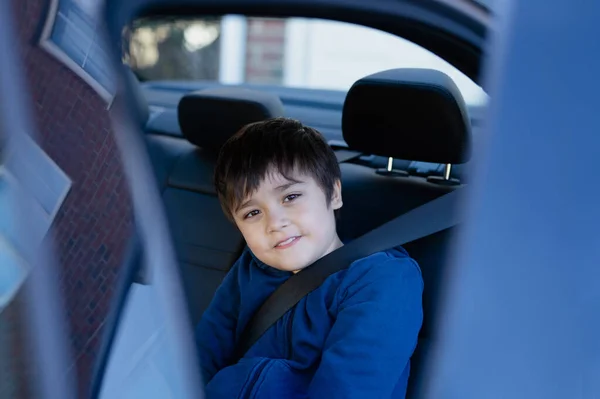 Cinematic portrait boy siting in safety car seat looking at camera with smiling face,Child sitting in the back passenger seat with a safety belt, School kid traveling to school by car.Back to school