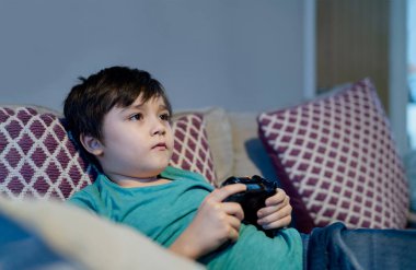 Mutlu çocuk video oyunu ya da oyun konsolu tutuyor. Çocuk okul kapalıyken evde oyun oynarken eğleniyor, çocuk evde kalıyor, karantina ve sosyal mesafe ya da kendini izole etme süresince evde kalıyor.