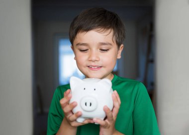 Gülümseyen yüzlü domuz kumbarasını tutan mutlu çocuk. Tasarruf kutusunu gösteren neşeli bir çocuğun yakın portresi. Okul çocuğu mali sorumluluk öğreniyor ve gelecek için para biriktirmeyi planlıyor.