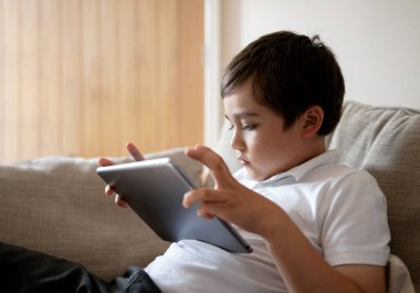 İnternette tablet kullanan okul çocuğu, oyun oynayan çocuk ya da dijital ekranda çizgi film izleyen çocuk, evde dinlenen mutlu çocuk, teknoloji ve sosyal ağ konsepti olan çocuklar.