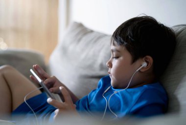 Öğrenci kulaklık kullanıyor. İnternetten tablet dersini dinliyor. Karışık ırk çocuğu kanepede oturup dijital bloknottan ödev yapıyor. Genç çocuk evde internetten öğreniyor ya da okuyor. Okul konseptine geri dönüyor.