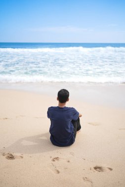 a man in a blue shirt, sitting enjoying the beautiful and clean beach.