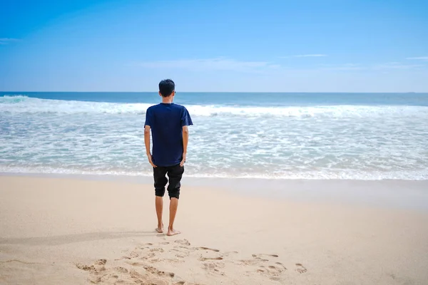 a man in a blue shirt, looking at the sandy beach in need, beautiful and clean.