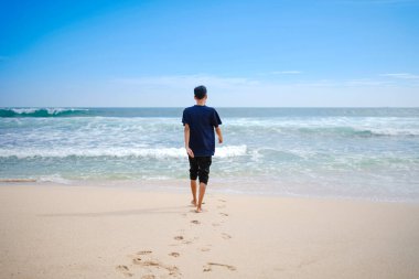 a man in a blue shirt, looking at the sandy beach in need, beautiful and clean.