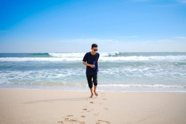 a man in a blue shirt, being chased by the waves. This beach looks beautiful, clean and white sand.