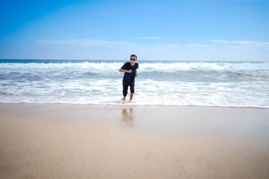 a man in a blue shirt, being chased by the waves. This beach looks beautiful, clean and white sand.