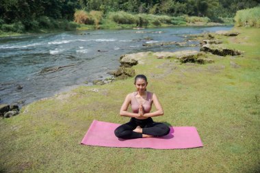 Zihinsel ve fiziksel sağlık. Sıska, bronz tenli Asyalı bir kadın sabahları sakin bir nehirde yoga yapıyor. Kadın Sukhasana pozu veriyor, meditasyon pozu..
