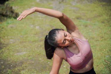 Sıska, bronz tenli bir Asyalı kız sabahları güzel bir nehir kenarında yoga pozu veriyor. Tema, sağlık, zihinsel ve fiziksel refah üzerine meditasyon..