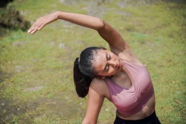 Sıska, bronz tenli bir Asyalı kız sabahları güzel bir nehir kenarında yoga pozu veriyor. Tema, sağlık, zihinsel ve fiziksel refah üzerine meditasyon..