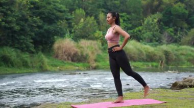 Bacak sallama kası yapan kız nehir altyapısı ile doğada esneme hareketleri yapıyor. Yüksek kalite 4k görüntü