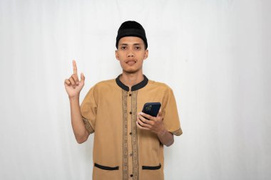 Geleneksel bir kıyafet giymiş genç bir Asyalı adam elinde telefonla bir jest yapıyor.