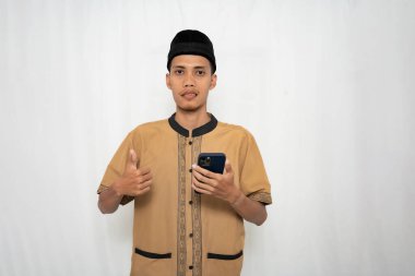 Geleneksel kıyafetler giyen genç bir adam akıllı telefon ve jestler tutuyor.