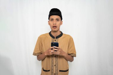 Geleneksel bir kıyafet giyen ve elinde akıllı telefon tutan siyah şapkalı bir gencin portresi.