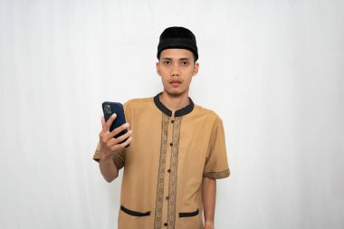 Geleneksel bir kıyafet ve şapka giyen genç bir adam elinde bir akıllı telefon tutuyor.
