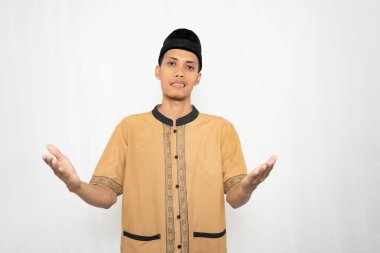 Geleneksel kıyafetler giyen genç bir adam, bir belirsizlik veya sorgulama jesti olarak omuzlarını silker.