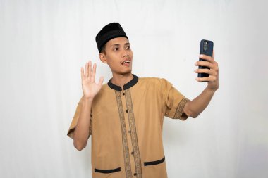 Geleneksel kıyafetler giymiş genç bir adam telefonuyla selfie çekiyor.