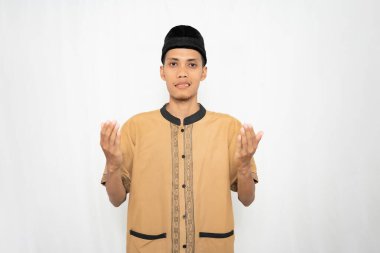 Siyah şapkalı ve geleneksel Müslüman kıyafetli genç bir adam elleriyle işaret ediyor.