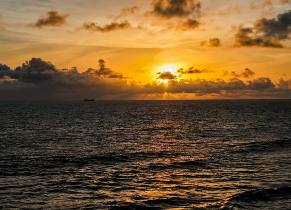 Canlı bir gün batımında bulutlarla birlikte huzurlu okyanus dalgaları.