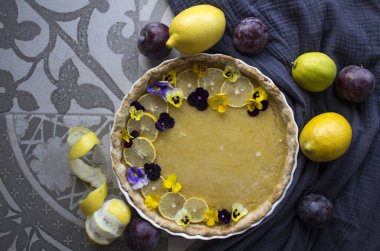 Limon dilimleri ve yabani nonoş çiçekleriyle süslenmiş limonlu tart. Klasik tatlı turtası üst görünümü fotoğrafı. 