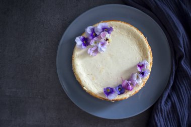 Mavi yabani nonoş çiçekleriyle süslenmiş ev yapımı cheesecake. Gri arkaplanda fotokopi alanı ile üstteki görüntü fotoğrafı.  