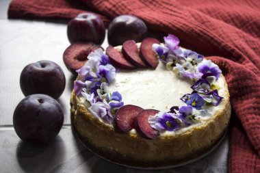 Kırmızı erikler ve yenilebilir çiçeklerle süslenmiş cheesecake. Kumaş dokusu arka planı. Ev yapımı tatlının en iyi görüntüsü.. 