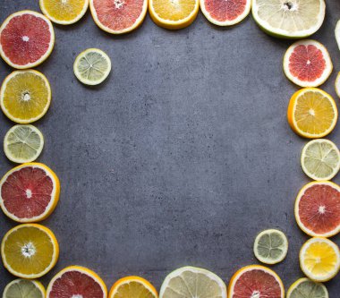 Meyve çerçevesi ya da kenar. Taze portakal, limon ve greyfurt dilimleri masada. Fotokopi alanı olan koyu gri arkaplan. Sağlıklı yeme kavramı.  