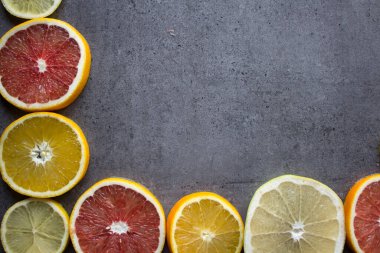 Meyve çerçevesi ya da kenar. Taze portakal, limon ve greyfurt dilimleri masada. Fotokopi alanı olan koyu gri arkaplan. Sağlıklı yeme kavramı.  