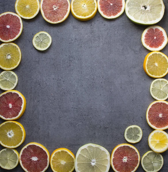 Fruit frame or border. Fresh juicy orange, lemon and grapefruit slices on a table. Dark gray background with copy space. Healthy eating concept.