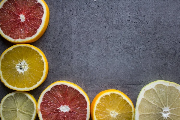 Fruit frame or border. Fresh juicy orange, lemon and grapefruit slices on a table. Dark gray background with copy space. Healthy eating concept.