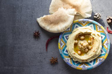 Humus gri masada renkli bir tabakta. Orta Doğu 'nun geleneksel yemekleri. Kopyalama alanı olan karanlık bir arkaplan. Sağlıklı yeme kavramı.