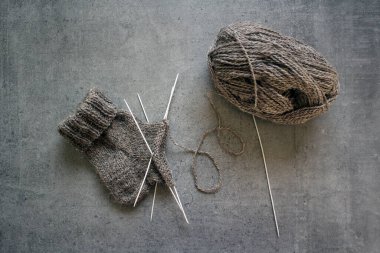 Çorap örüyorum, çalışıyorum. Yün ipliği, örgü iğneleri ve el yapımı çorabın yarısı. Gri desenli arka plan. Kış hobileri. 