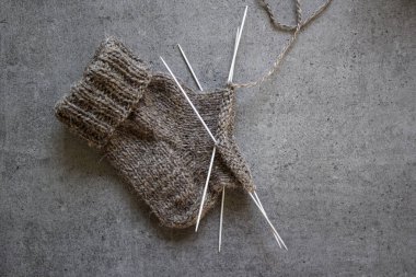 Çorap örüyorum, çalışıyorum. Yün ipliği, örgü iğneleri ve el yapımı çorabın yarısı. Gri desenli arka plan. Kış hobileri. 