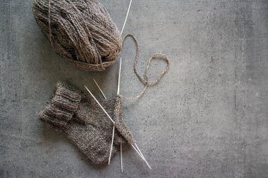Çorap örüyorum, çalışıyorum. Yün ipliği, örgü iğneleri ve el yapımı çorabın yarısı. Gri desenli arka plan. Kış hobileri. 