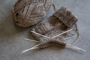 Çorap örüyorum, çalışıyorum. Yün ipliği, örgü iğneleri ve el yapımı çorabın yarısı. Gri desenli arka plan. Kış hobileri. 