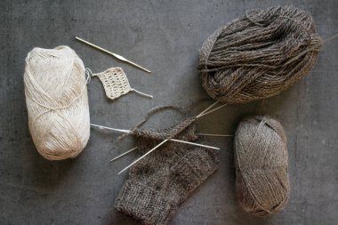 Çorap örüyorum, çalışıyorum. Yün ipliği, örgü iğneleri ve el yapımı çorabın yarısı. Gri desenli arka plan. Kış hobileri. 