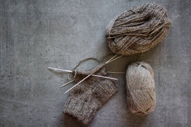 Çorap örüyorum. İğne işi devam ediyor. Doğal yünden yapılmış kahverengi çorap, iğneler ve iplik yumakları. Kopyalama alanı olan gri arkaplan. 