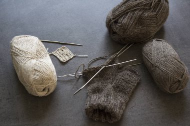 Çorap örüyorum. İğne işi devam ediyor. Doğal yünden yapılmış kahverengi çorap, iğneler ve iplik yumakları. Kopyalama alanı olan gri arkaplan. 